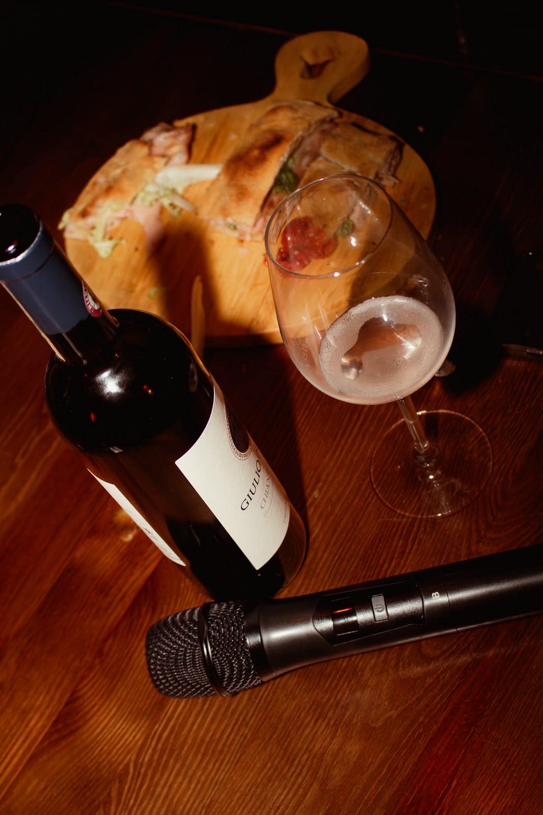 Bottiglia di vino, calice e microfono su un tavolo di legno accanto a un tagliere di panini