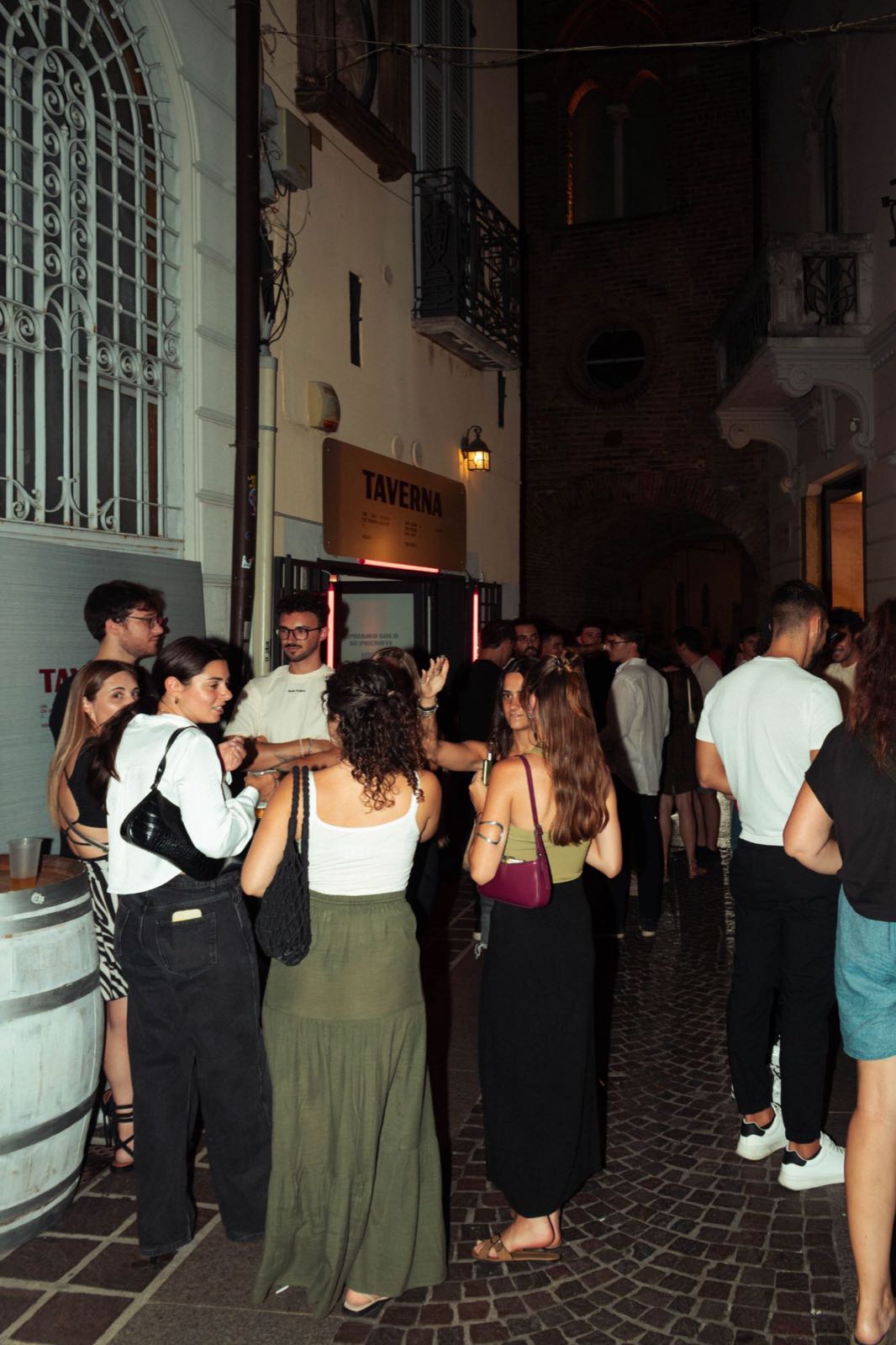 Amici si ritrovano in strada davanti all'ingresso della Taverna in una serata d'estate